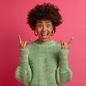 happy carefree dark skinned rebellious young woman enjoys awesome music makes rock n roll gesture has fun on music festival or cool event wears casual jumper poses against pink wall Home digital marketing